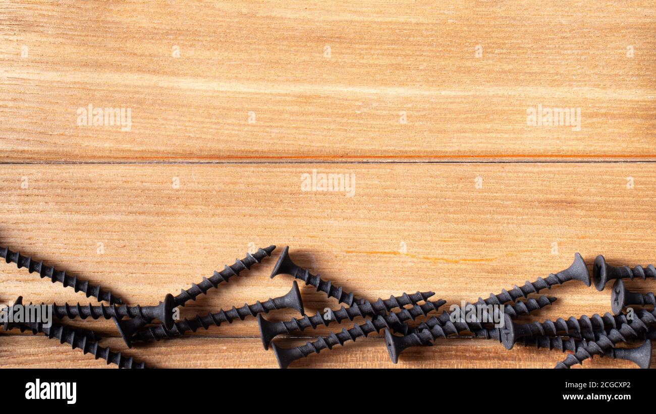 Self-cutters on a wood brown background banner with space for text. Construction tools, self-tapping screws for fastening. Black screw hardware Stock Photo