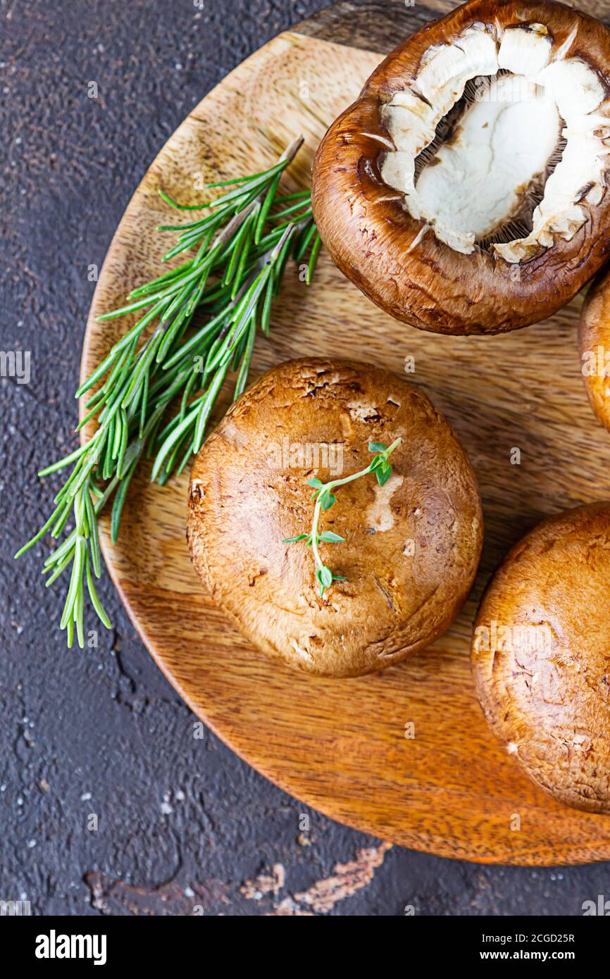 Fresh delicious portobello mushrooms with thyme and rosemary on wooden cutting board, dark stone background. Top view. Stock Photo