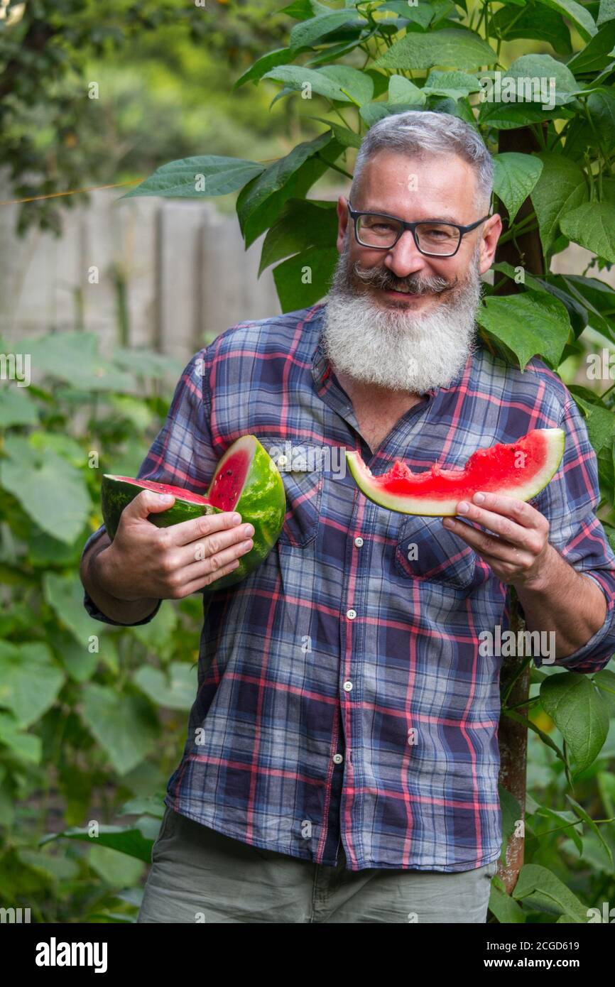 Portrait of mature bearded male farmer with ripe watermelon, own harvest concept, selective focus Stock Photo