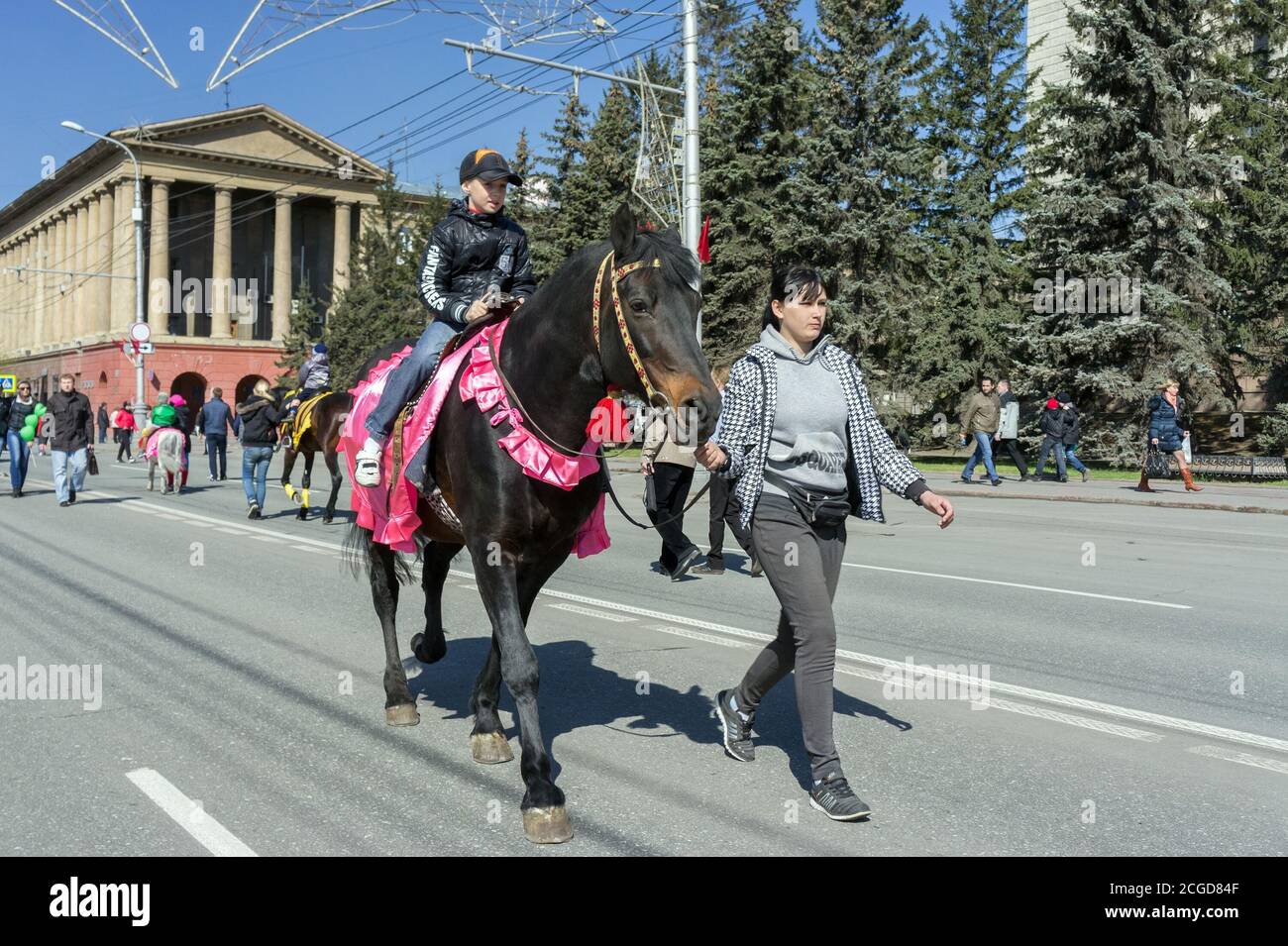 Boy rides on a smart brown horse driven by a girl along the avenue of Krasnoyarsk city during the celebration of Victory Day WWII. Stock Photo