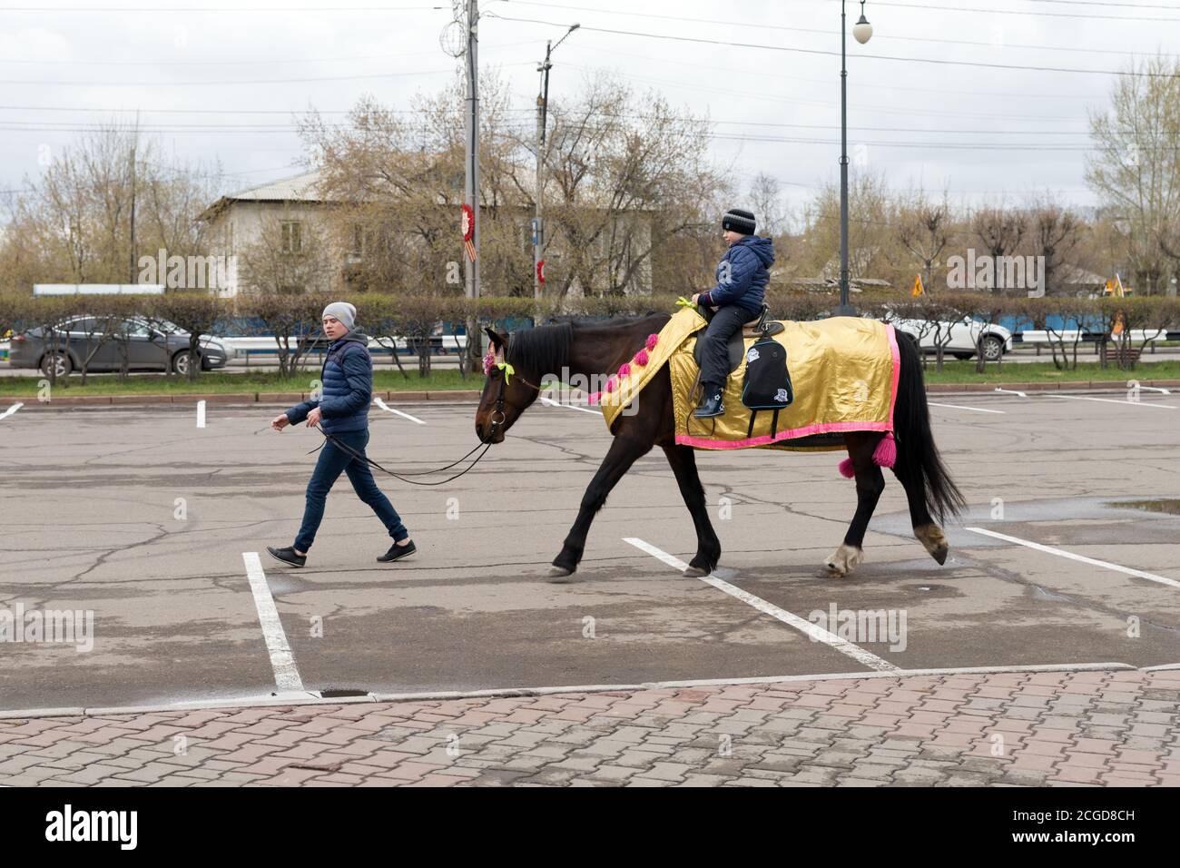 A young man leads an elegant horse, on which a boy rides on the street, during the celebration of Victory Day WWII. Krasnoyarsk. Stock Photo