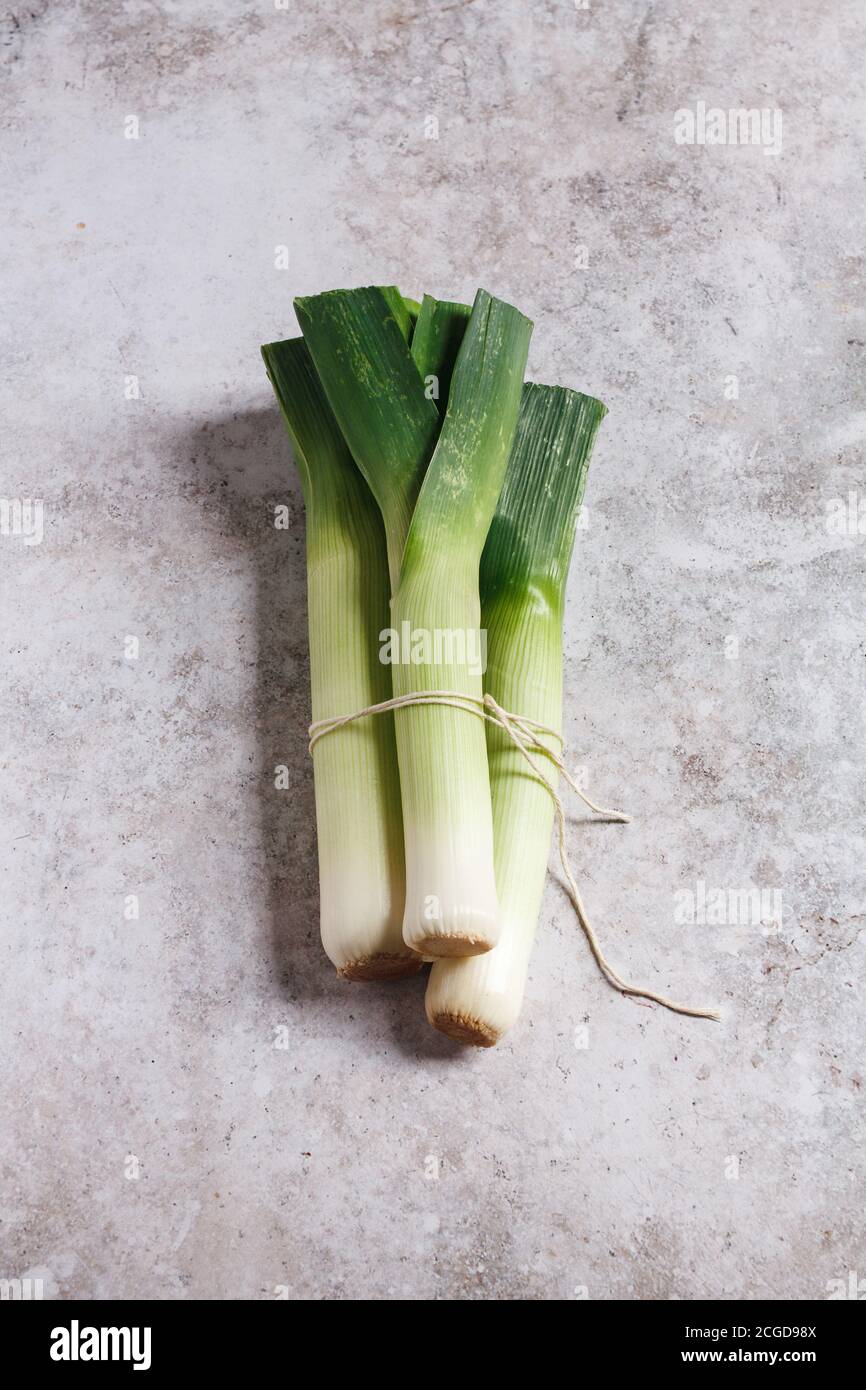 Three fresh leeks tied together with white twine on a grey textured table top. Stock Photo