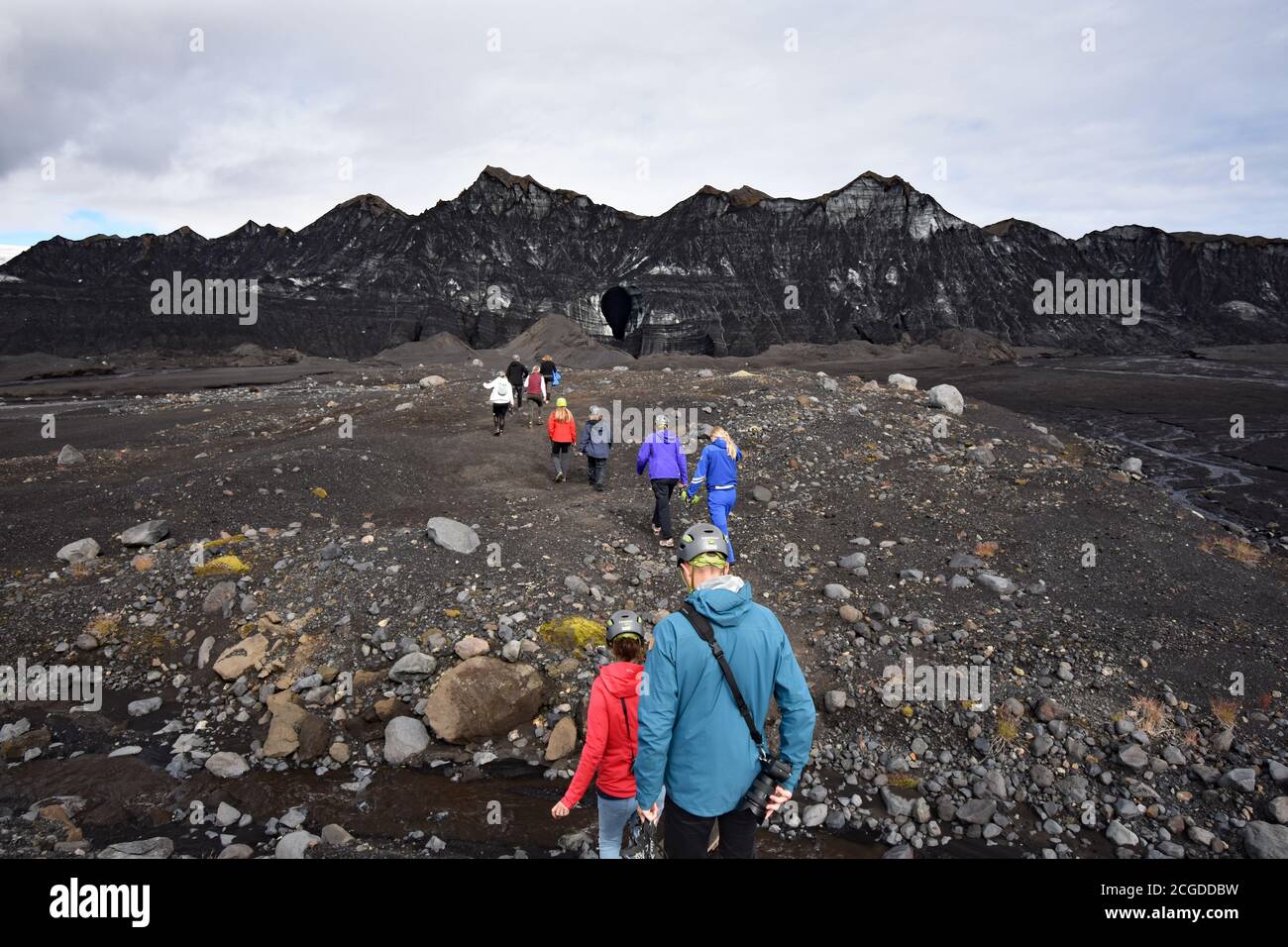 A tour group walks towards the Katla Ice Cave in Kotlujokull Glacier, an outlet glacier of Myrdalsjokull. The glacier is covered in volcanic ash. Stock Photo