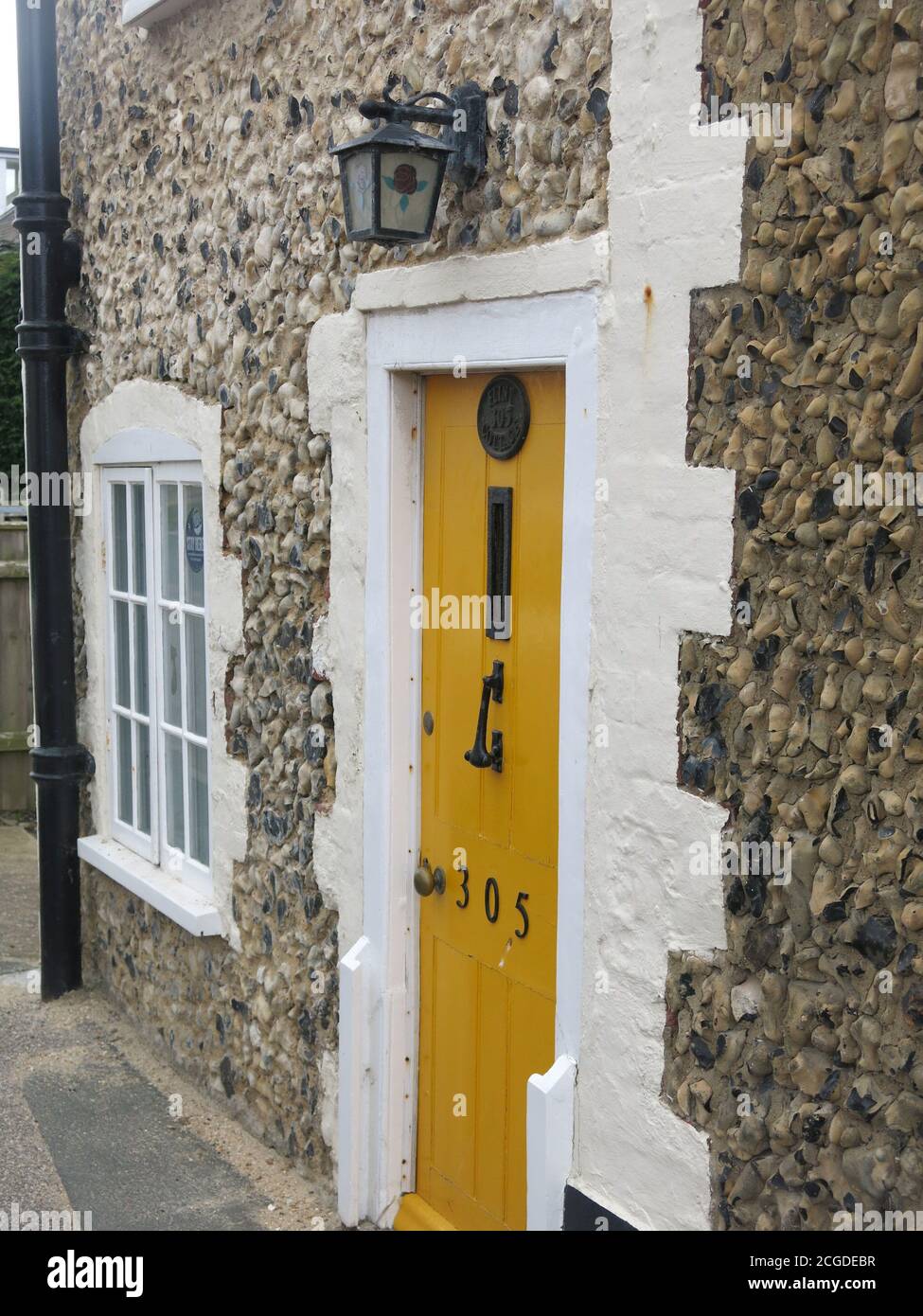 Terraced house number 305 with a mustard yellow front door & shingle pebble dashing on the exterior walls; typical seaside cladding for Suffolk houses Stock Photo
