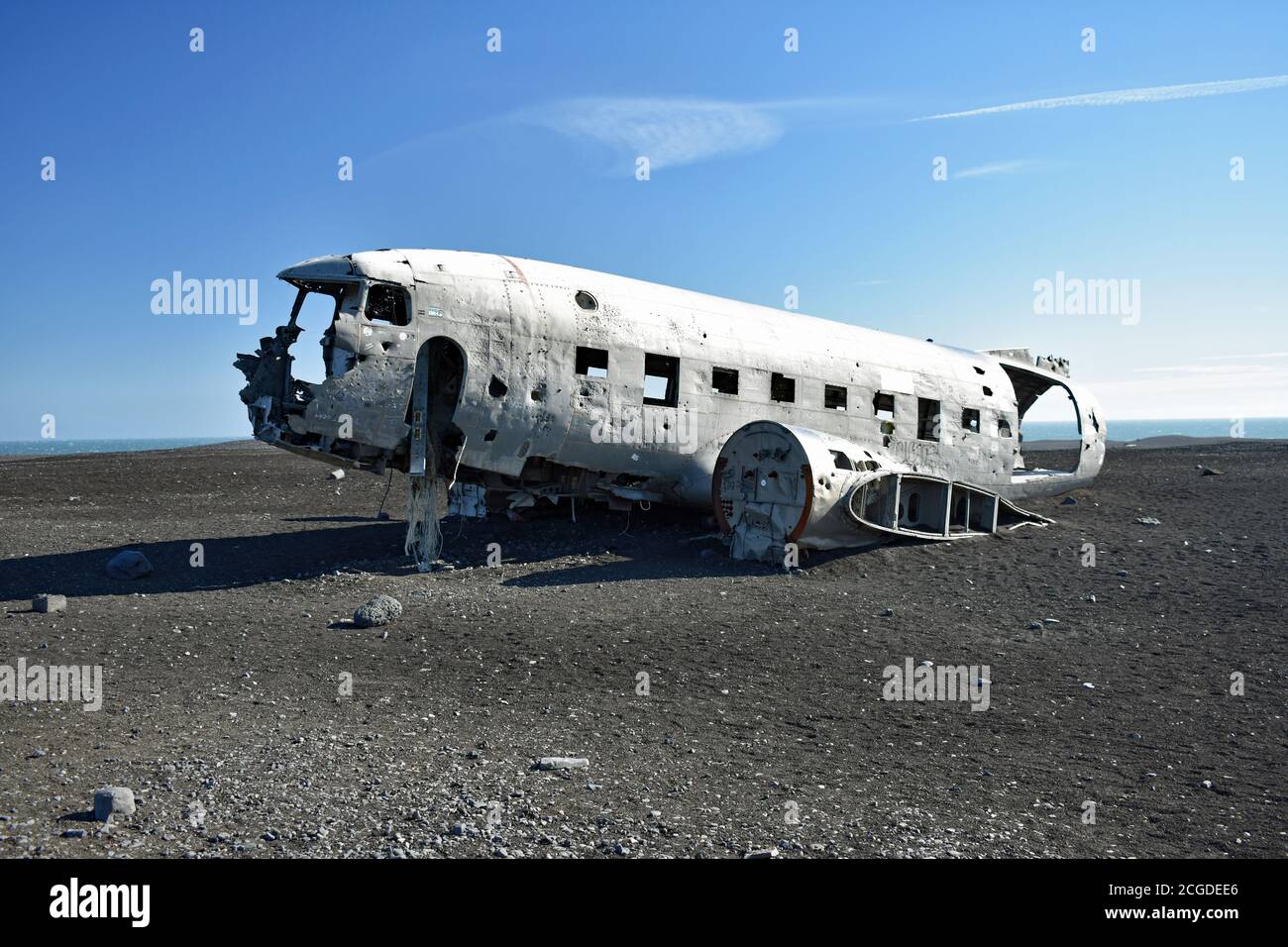 The fuselage of the Solheimasandur Plane Wreck sits on the black sand glacial outwash plains of Myrdalsjokull on a clear sunny day with blue sky. Stock Photo