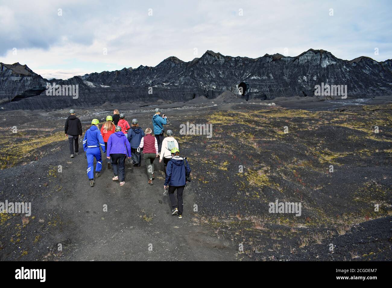 A group of tourists walk across the black volcanic sand towards Kotlujokull Glacier, an outlet glacier of Myrdalsjokull on an overcast day. Iceland. Stock Photo