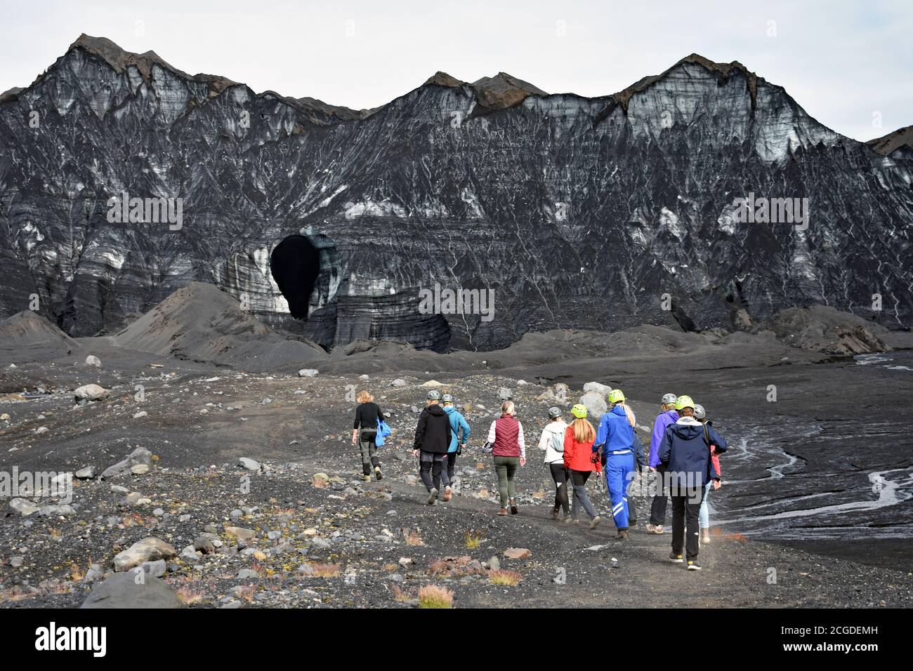 A group tour in brightly coloured clothing walk up to the black volcanic sand covered Kotlujokull Glacier, an outlet glacier of Myrdalsjokull. Iceland Stock Photo