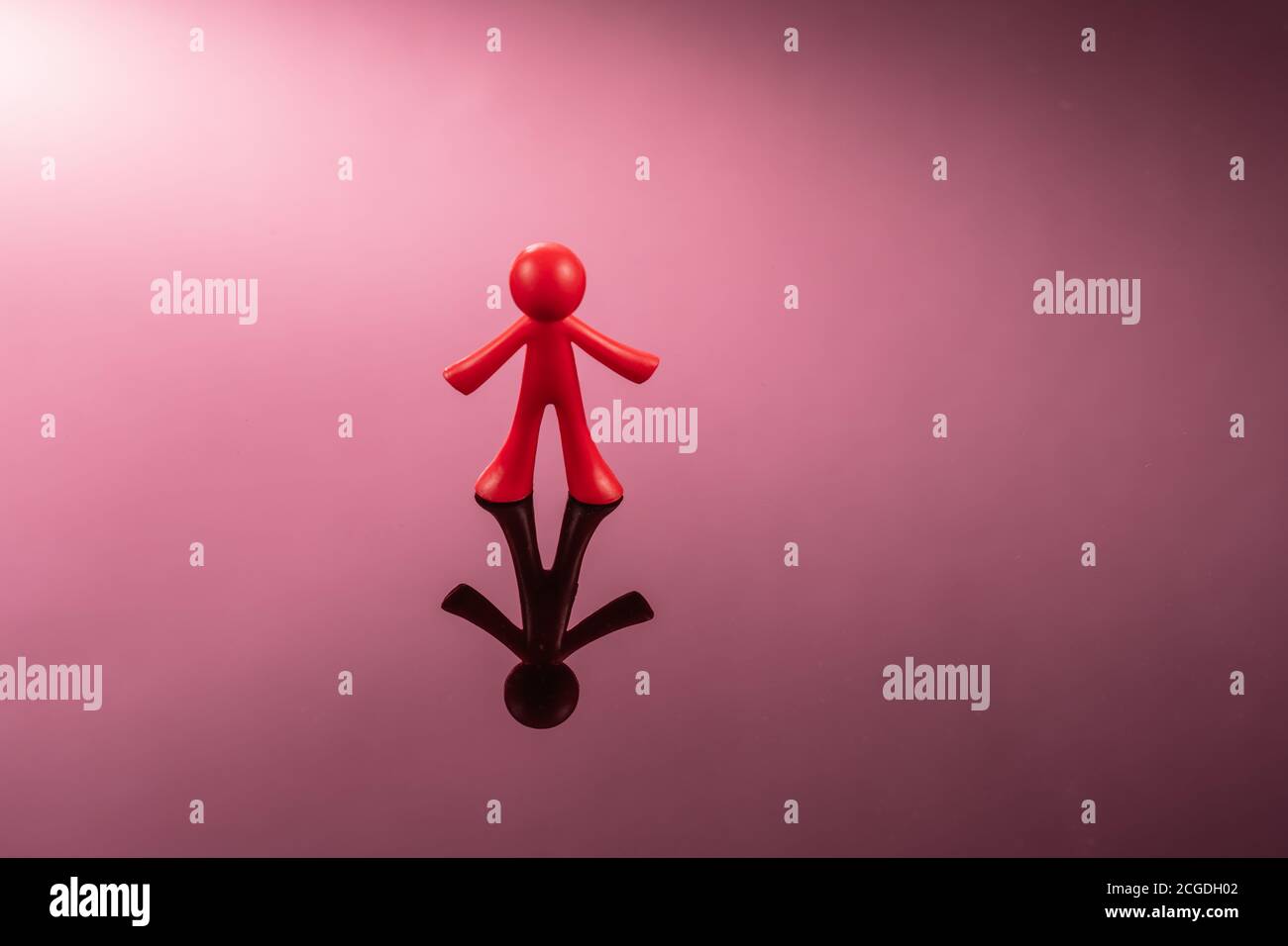 Red plastic figure of a man standing on a mirror pink surface Stock Photo