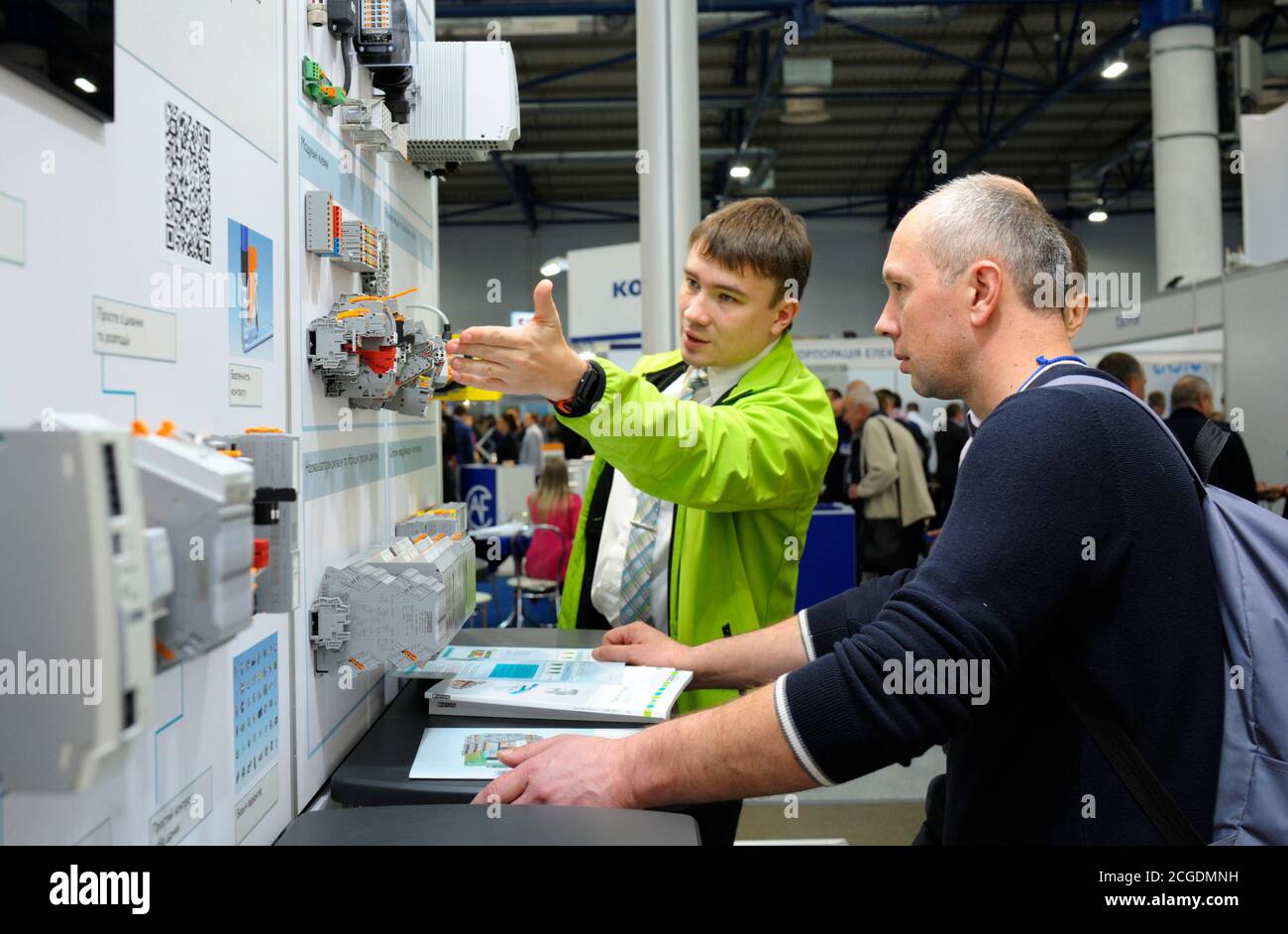 Manager touching the block of the automatic control system of the power supply presented on the stand, explaining to the visitor. Exhibition Industria Stock Photo
