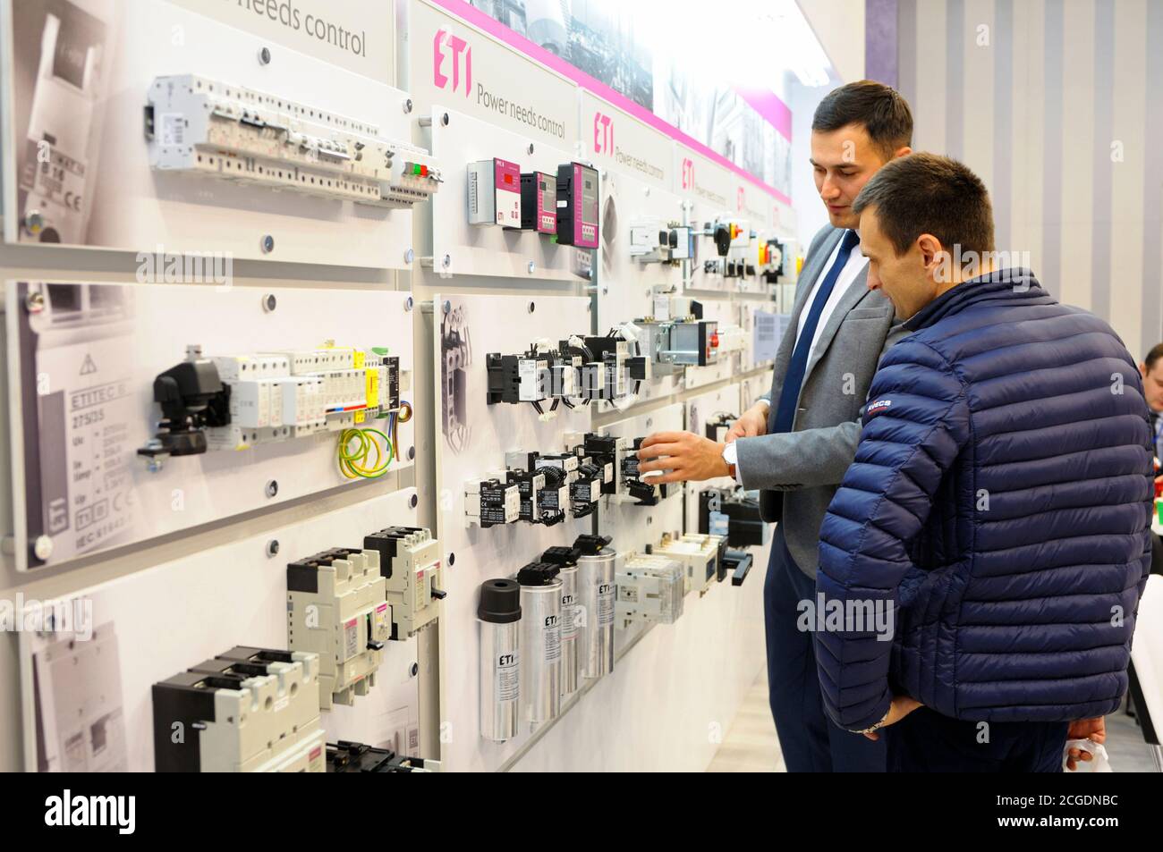 Manager touching the block of the automatic control system of the power supply presented on the stand, explaining to the visitor. Exhibition Industria Stock Photo