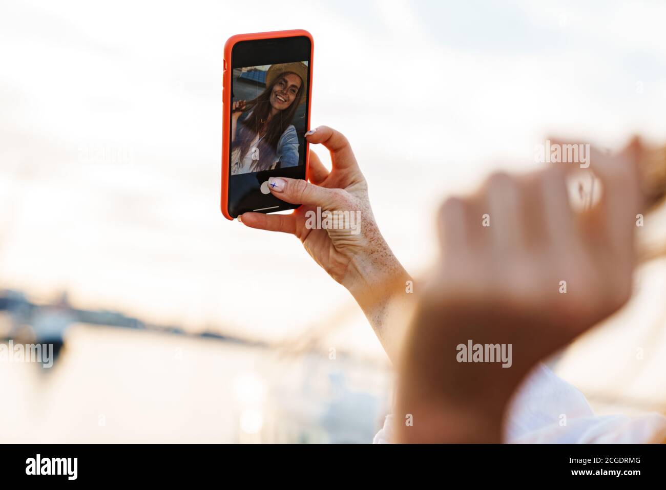 Image of laughing ginger woman smiling and taking selfie on mobile phone at promenade Stock Photo