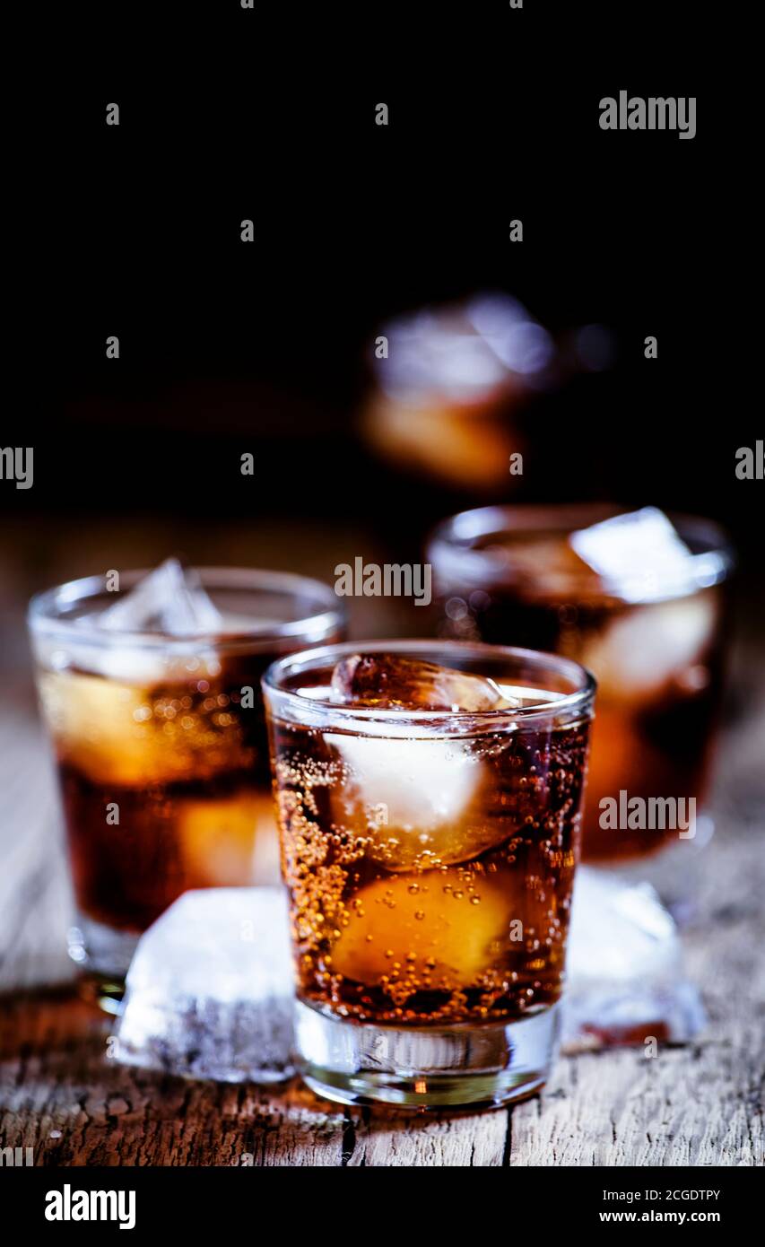 Alcoholic cocktail bourbon cola with whiskey and ice cubes, vintage wooden background, selective focus Stock Photo