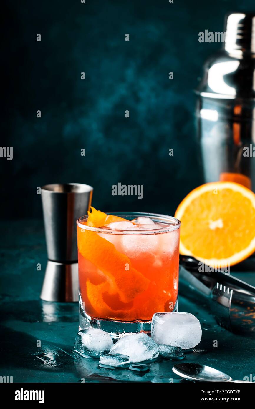Orange Alcohol cocktail with red vermouth, bitter, soda, orange zest and ice, dark wooden bar