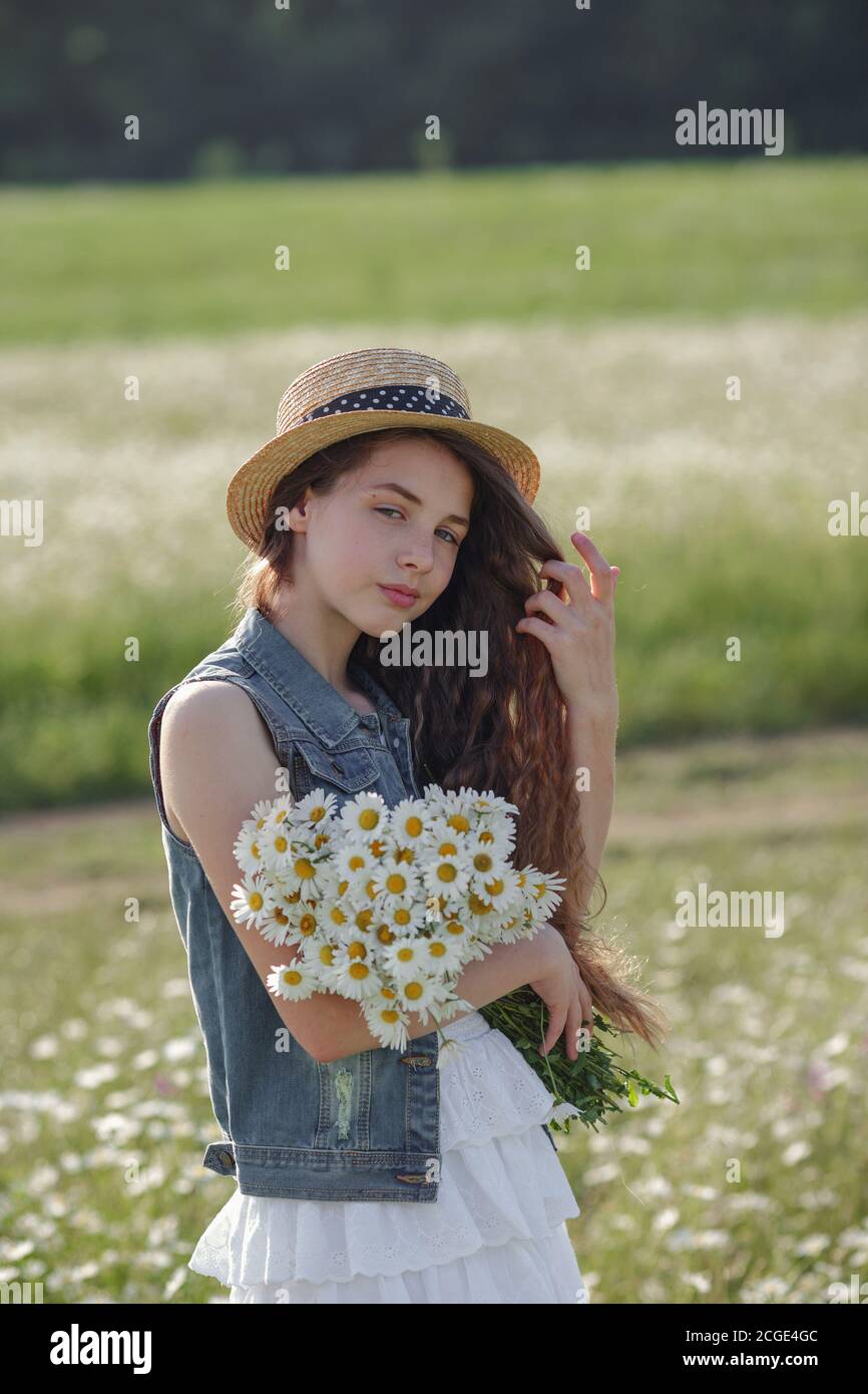 Beautiful teenage girl in a white dress and hat walking in a field of ...