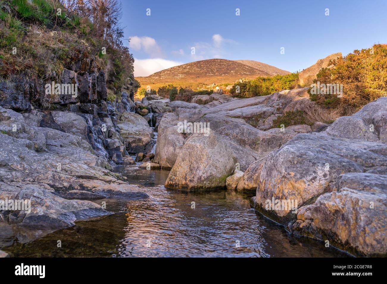 Mountain stream flowing between rocks with mountain peak of Slieve Donard, highlighted by sunlight in background, Mourne Mountains, Northern Ireland Stock Photo