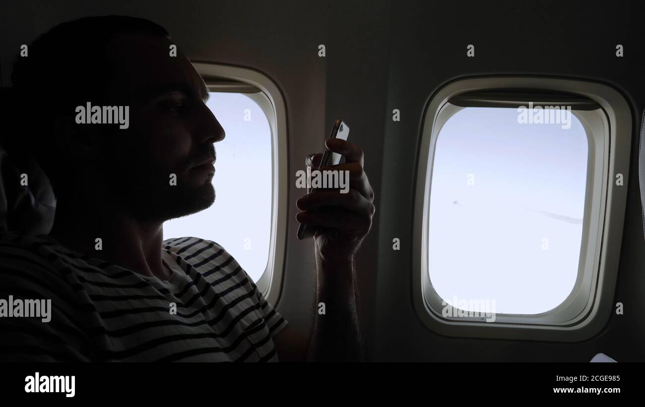 Man looking through pictures on his phone sitting in a plane. Stock Photo