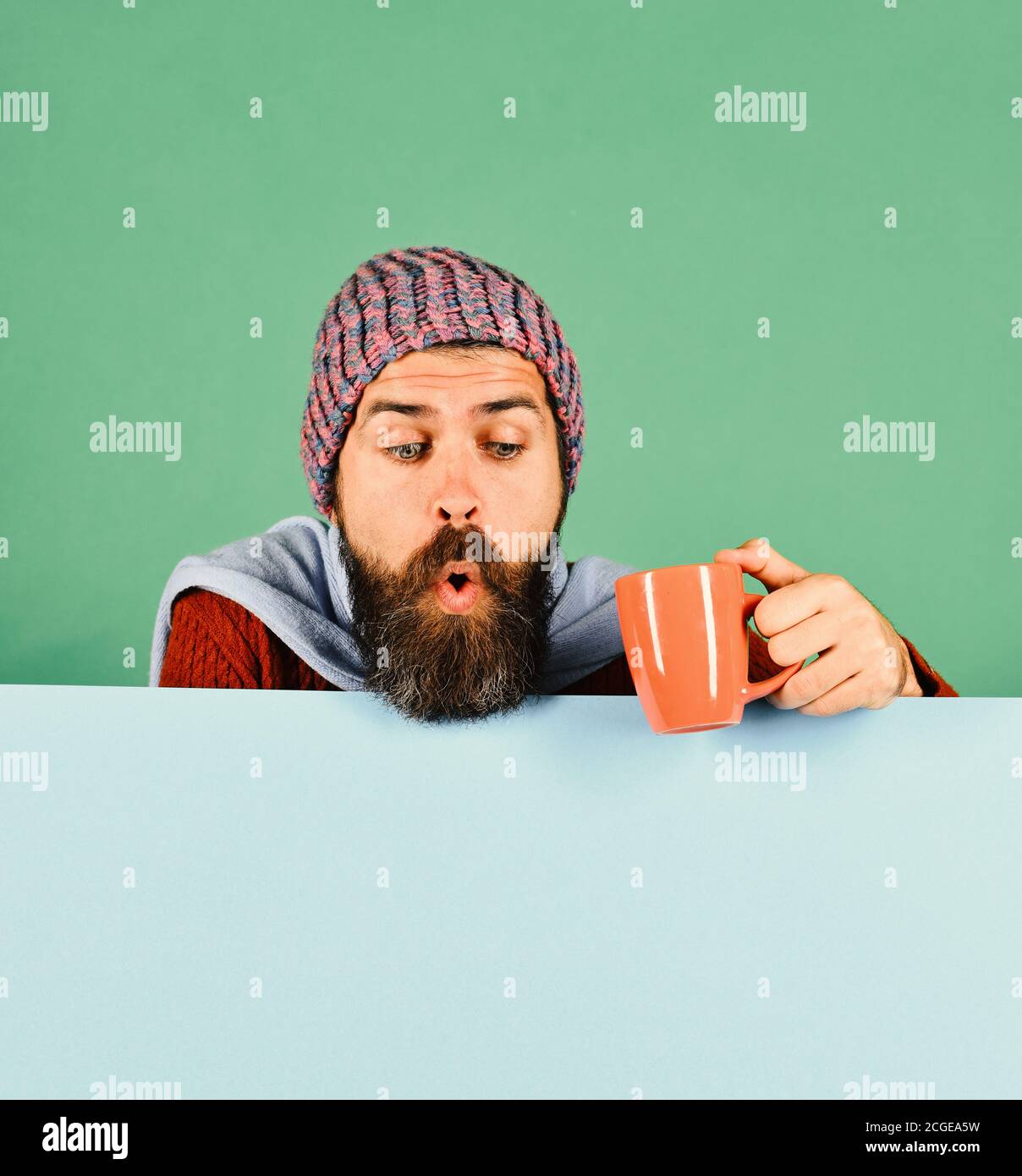 https://c8.alamy.com/comp/2CGEA5W/english-tea-and-autumn-concept-guy-with-surprised-face-looks-down-wearing-warm-hat-on-green-and-cyan-background-copy-space-fall-season-and-hot-beverage-time-man-with-beard-holds-orange-tea-cup-2CGEA5W.jpg
