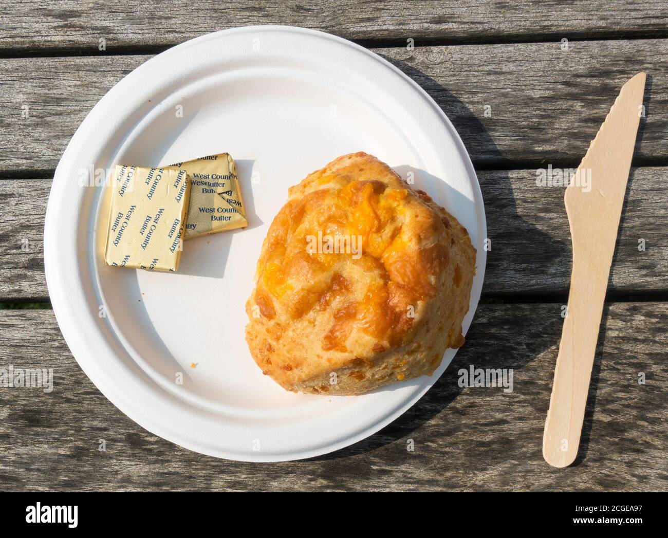 Cheese scone on disposable paper plate with wooden knife and pats of butter Stock Photo