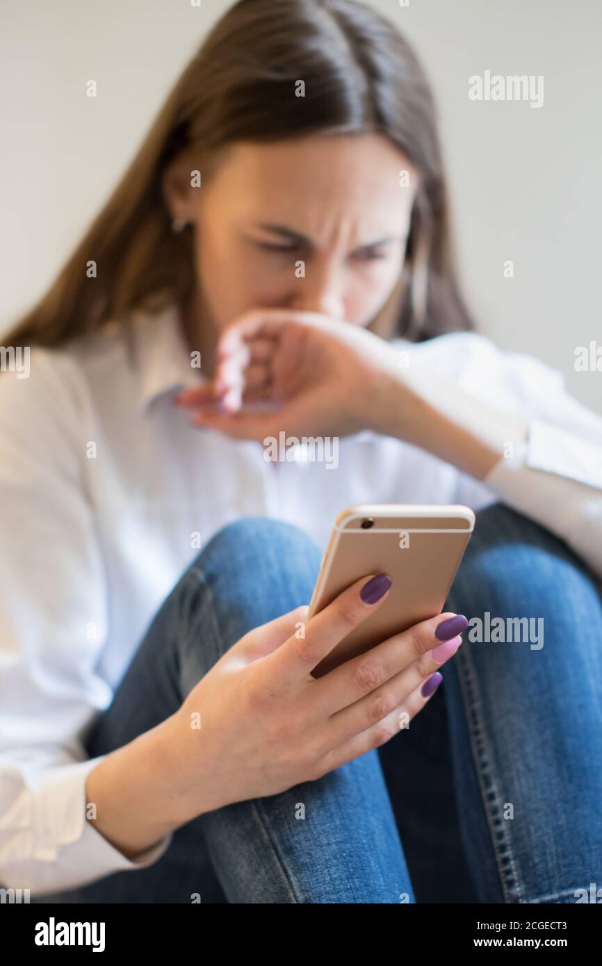 Crying woman in depression looking at phone gets bad news, covering mouth with hand, focus on the phone Stock Photo
