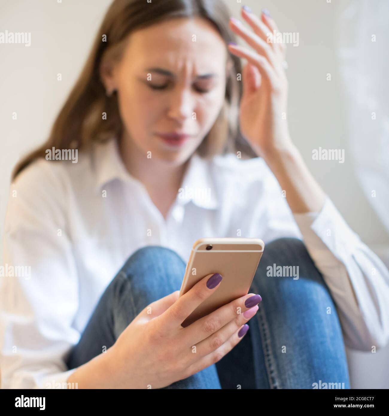 Crying woman in depression looking at phone gets bad news, sitting, focus on smartphone. Stock Photo