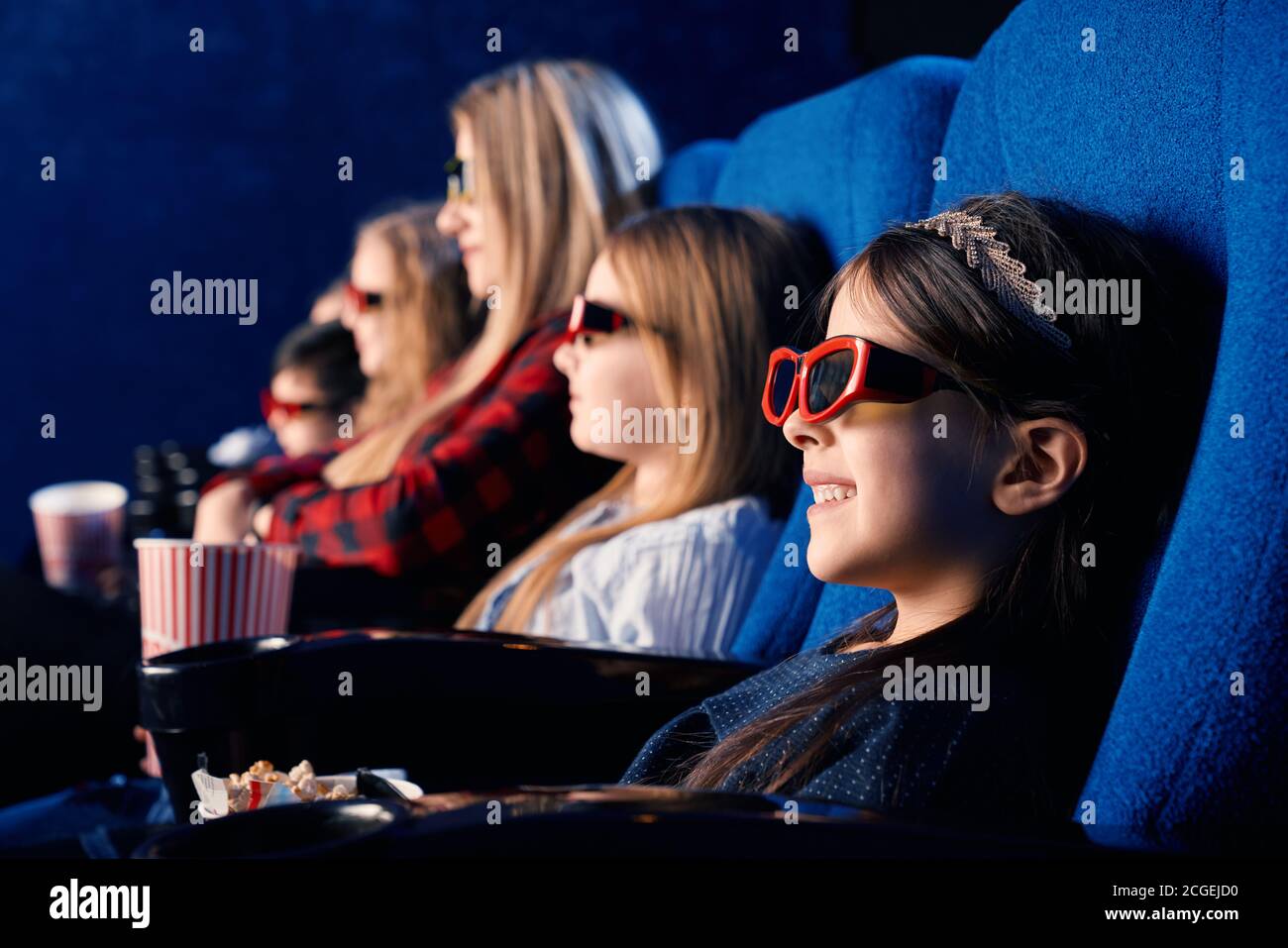 Selective focus of laughing child wearing 3d glasses, eating popcorn and watching funny movie. Cute little girl enjoying time with friends in cinema. Concept of leisure and entertainment. Stock Photo