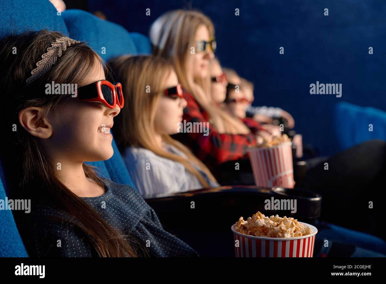 Selective focus of laughing child wearing 3d glasses, eating popcorn and watching funny movie. Cute little girl enjoying time with friends in cinema. Concept of leisure and entertainment. Stock Photo