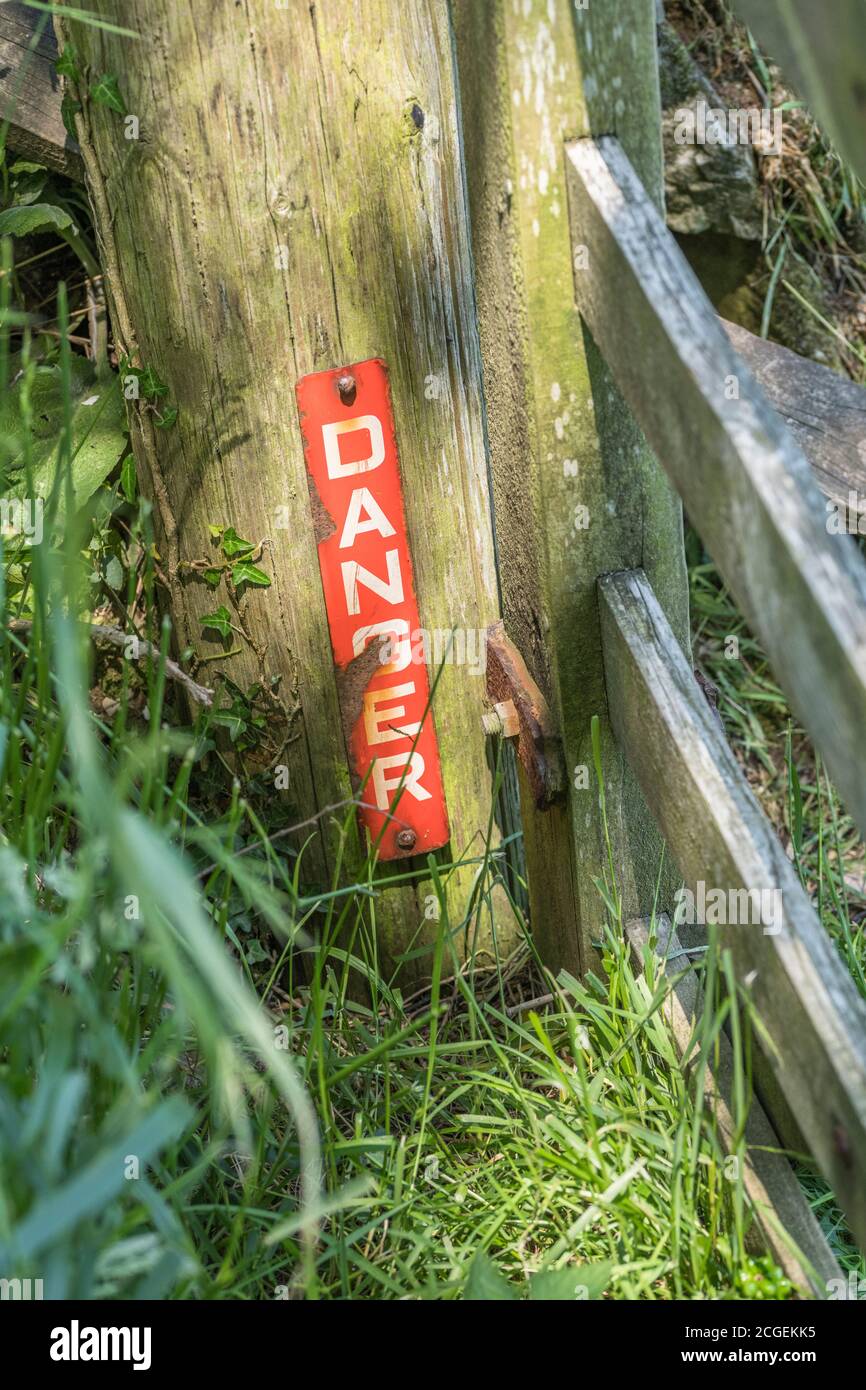 Red danger warning sign on wooden farm gate post. Presumably for a buried electricity cable or gas pipeline. Hidden danger, lurking danger, be warned. Stock Photo
