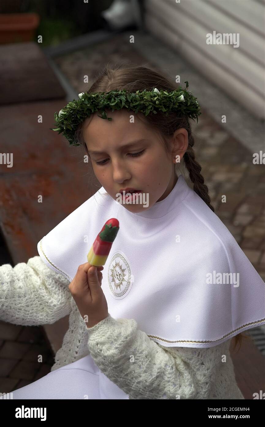 Girl in a white communion dress is eating ice cream on a stick. Ein Mädchen in einem weißen Kommunionkleid isst ein Eis am Stiel. Dziewczynka z lodem Stock Photo