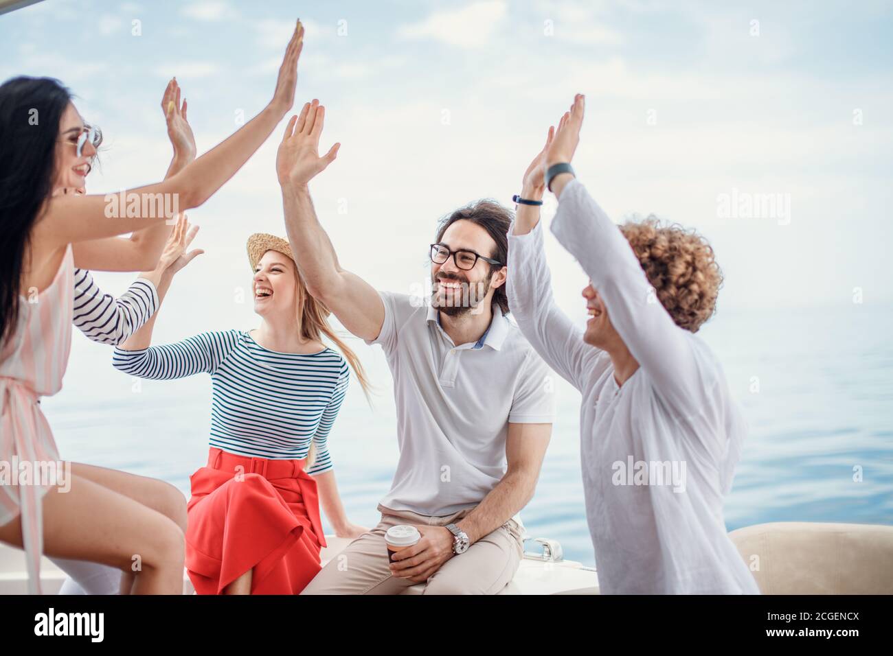 Group of friends, dressed in casual cloth, giving high five on a fashionable yacht - Happy people having a fancy party on a luxury boat Stock Photo