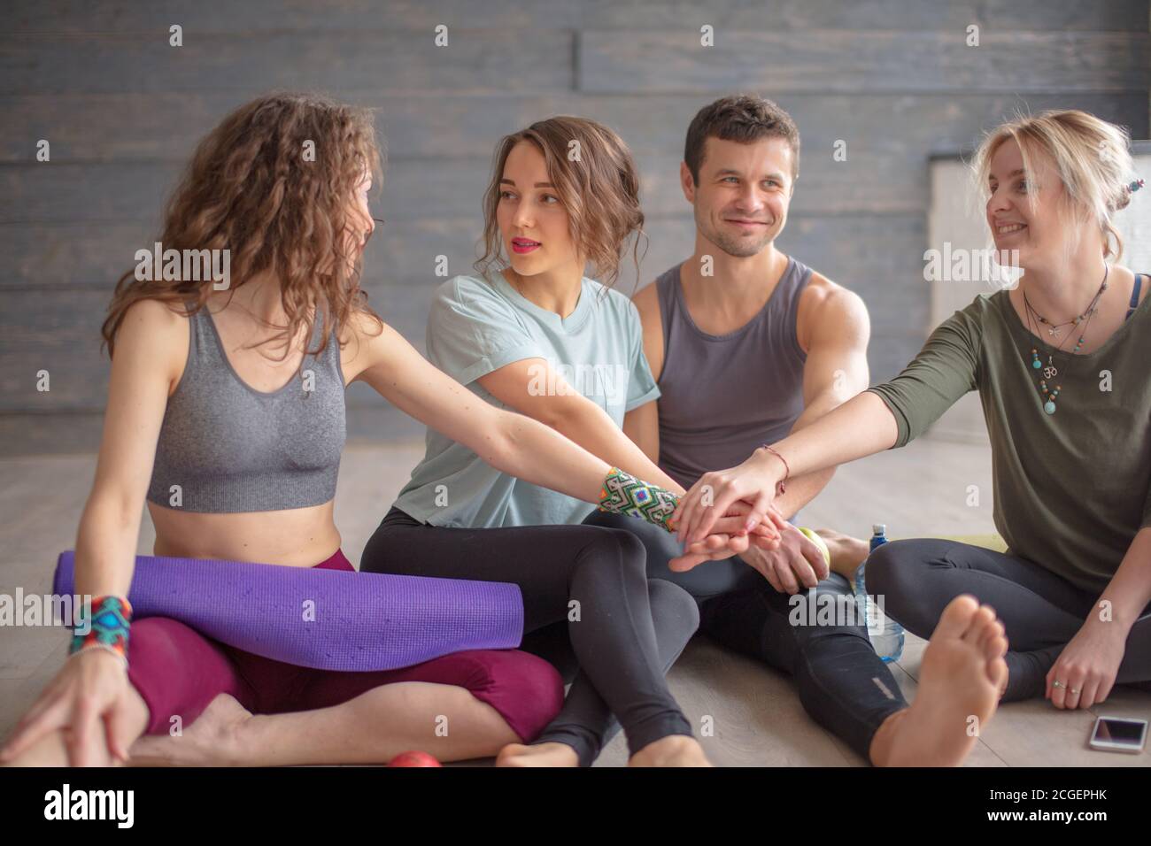 Group of female and male yoga pupils relaxing with fresh fruit and water after yoga training at health club. Friends checking messages and socialmedia Stock Photo