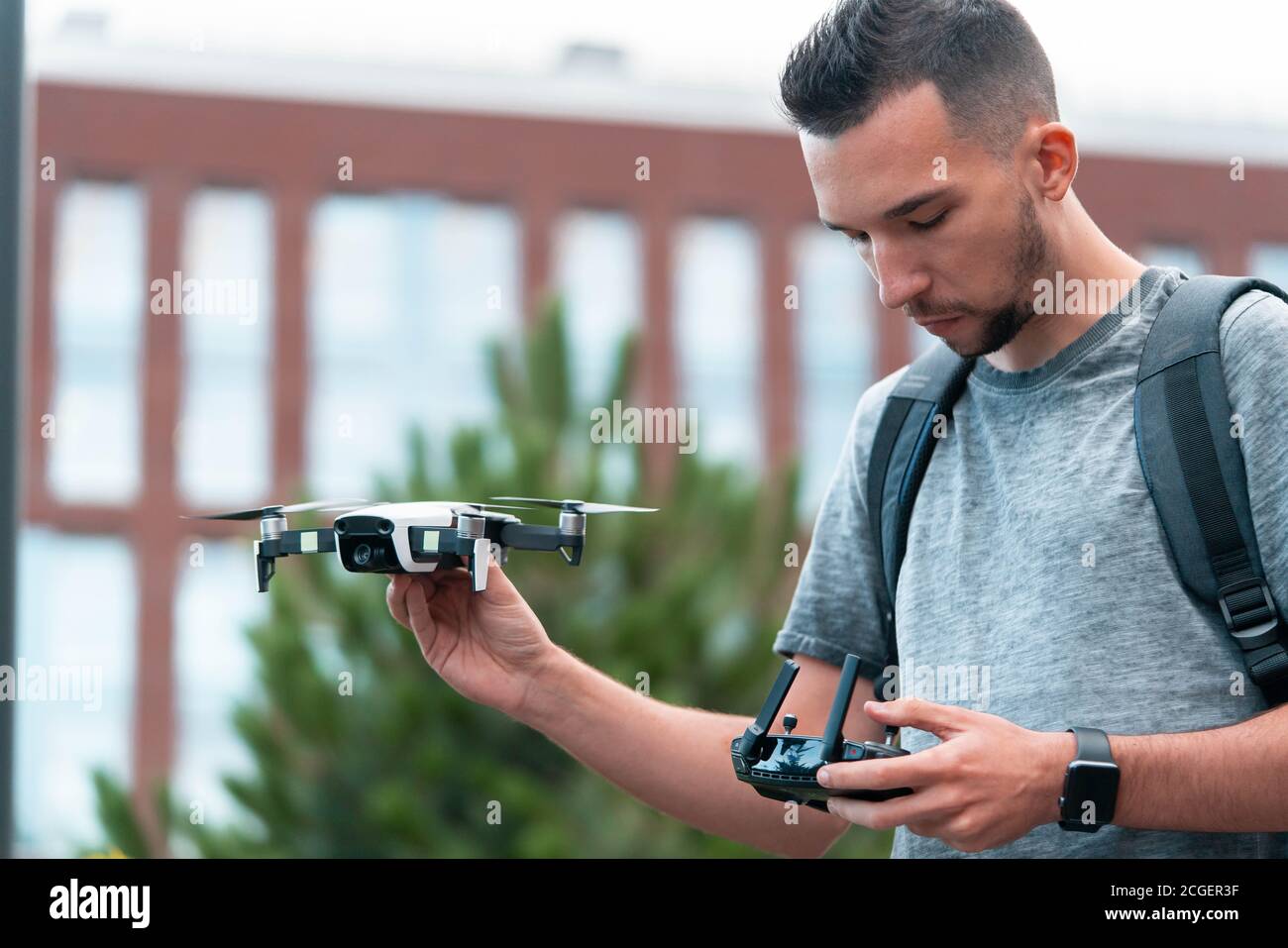 Young Handsome Brunette Man Launching Drone Quadcopter and Looking At Remote Controller Joystick. Urban Stlilysh Contemporary Cityscape. Modern device Stock Photo