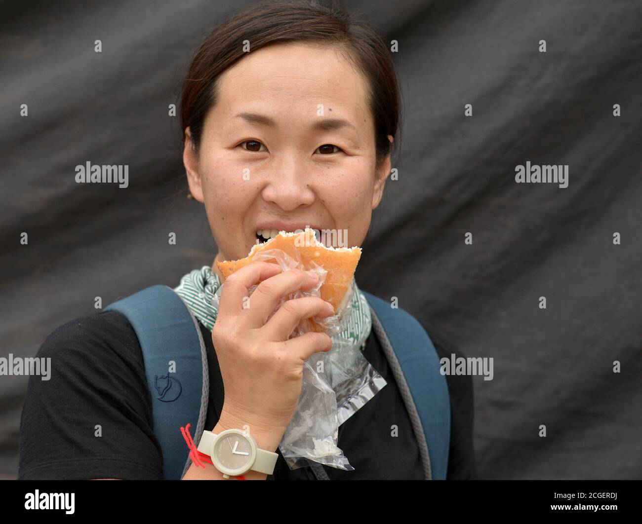 Female Japanese tourist eats a bread roll and looks at the camera. Stock Photo