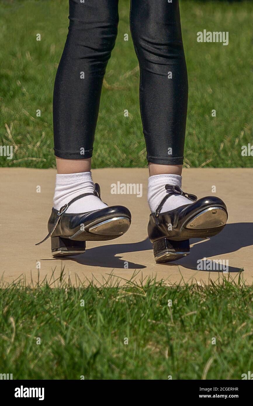 Legs and feet of young girl in black tap shoes, white socks and black tights. Dancing tap dance outdoors . Low angle shot. Close view. Stock Photo