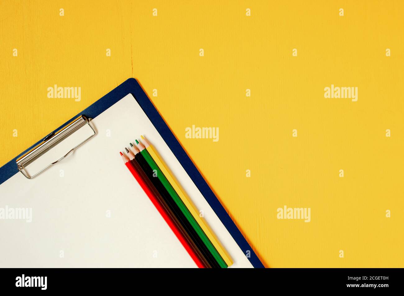 A paper tablet with a blank sheet and five colored wooden pencils on a bright yellow wooden background Stock Photo