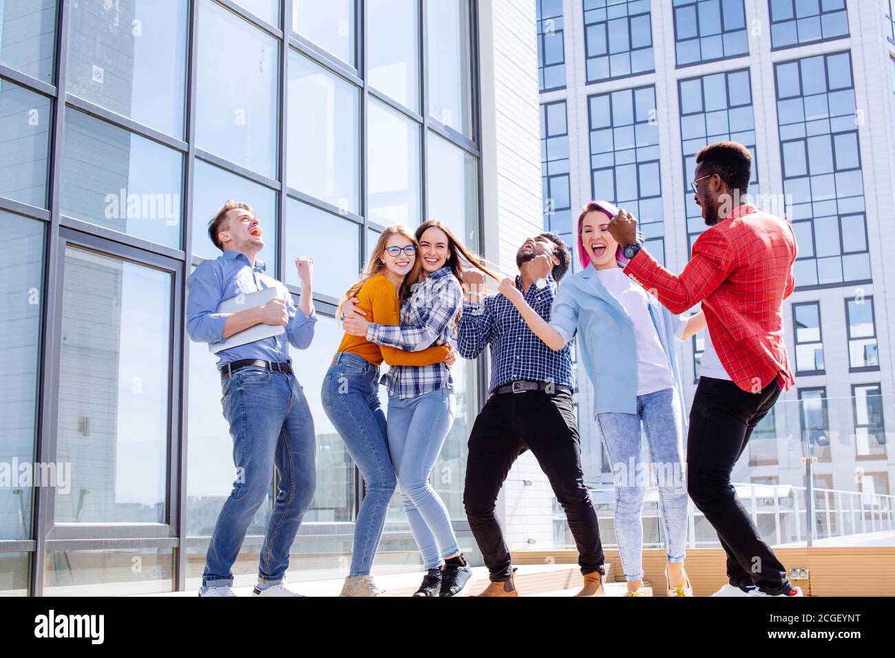 Group of multi ethnic young friends dressed in casual cloth having fun on lounge outdoor area on the roof of office glass building Stock Photo