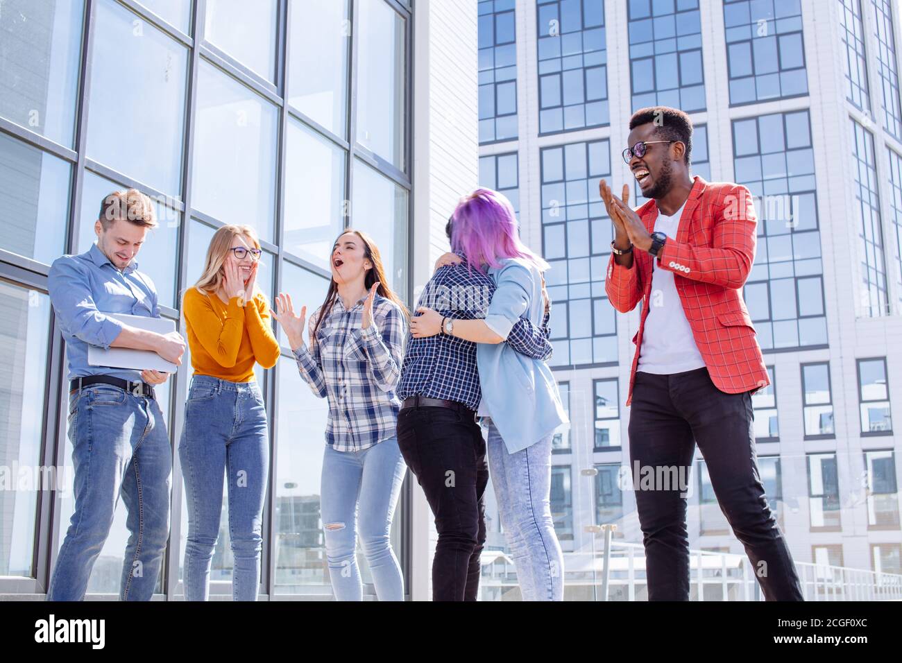 Group of multi ethnic young friends dressed in casual cloth having fun on lounge outdoor area on the roof of office glass building Stock Photo