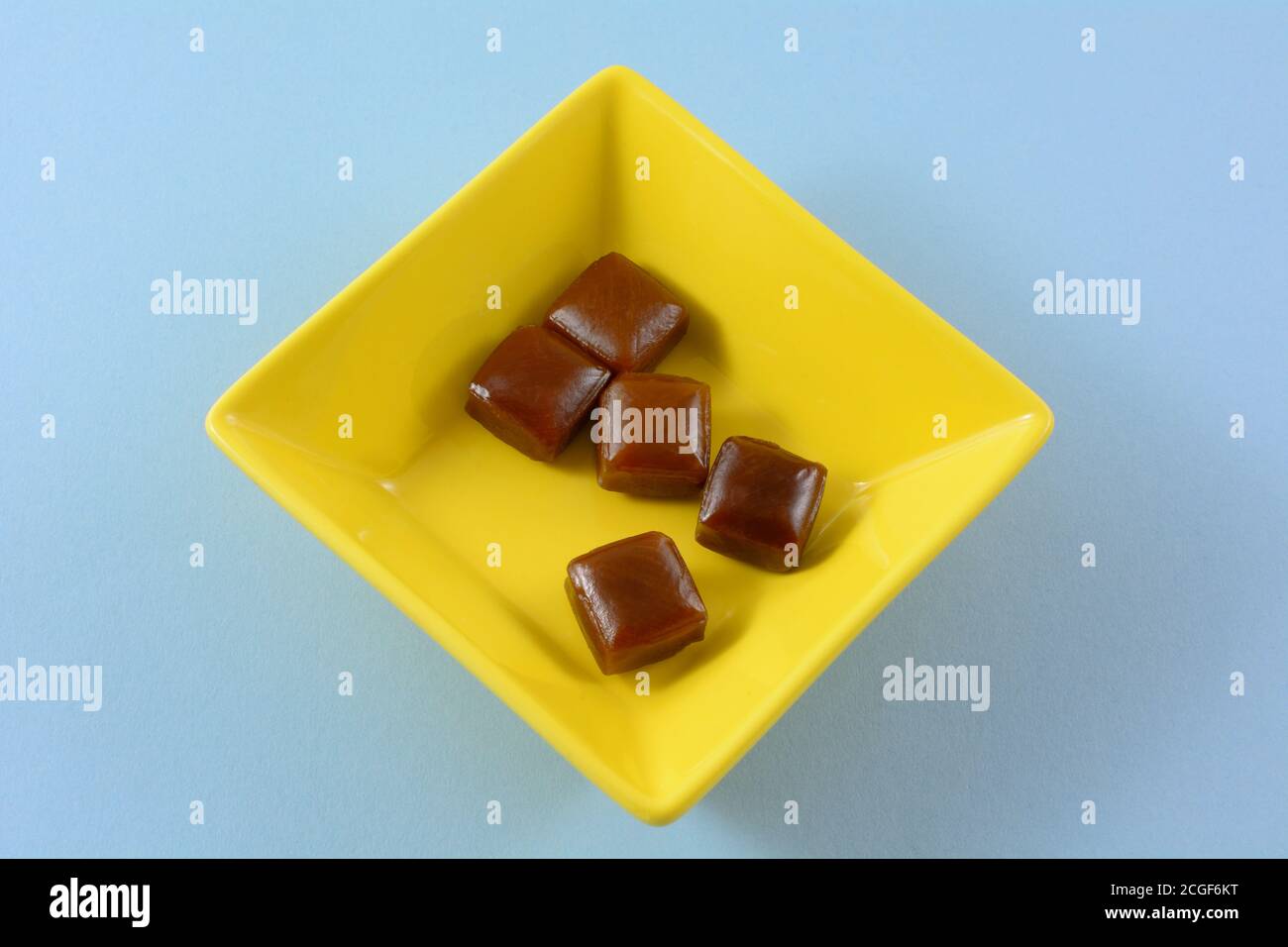 Coffee flavored hard candy in yellow candy dish on blue background Stock Photo