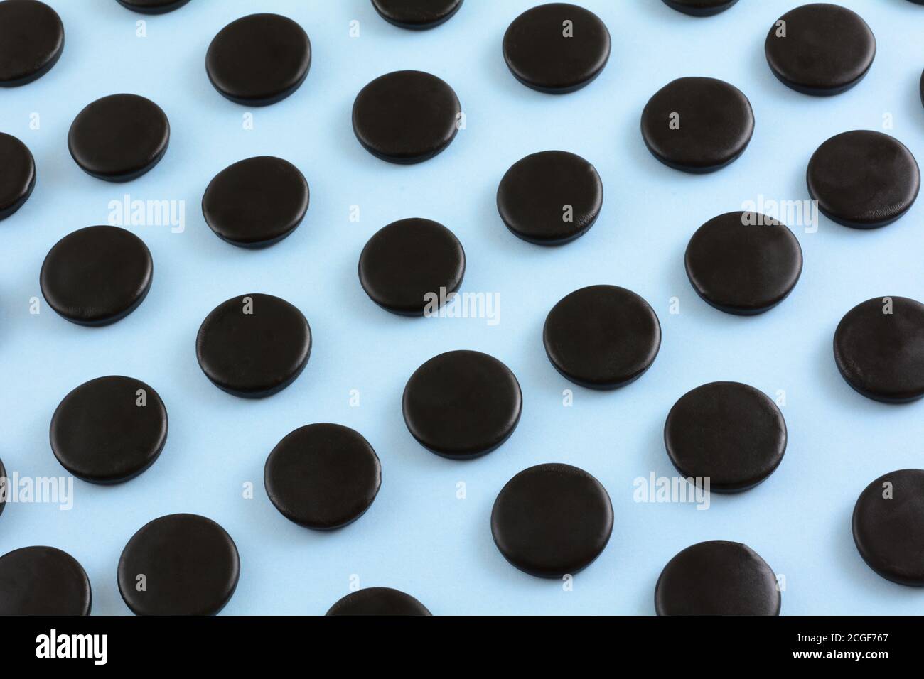 Black licorice candy coins in rows on light blue background Stock Photo