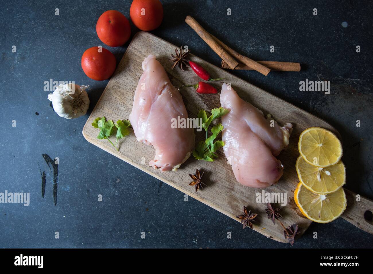 Raw chicken fillets on a wooden cutting board with ingredients for cooking on a black background Stock Photo
