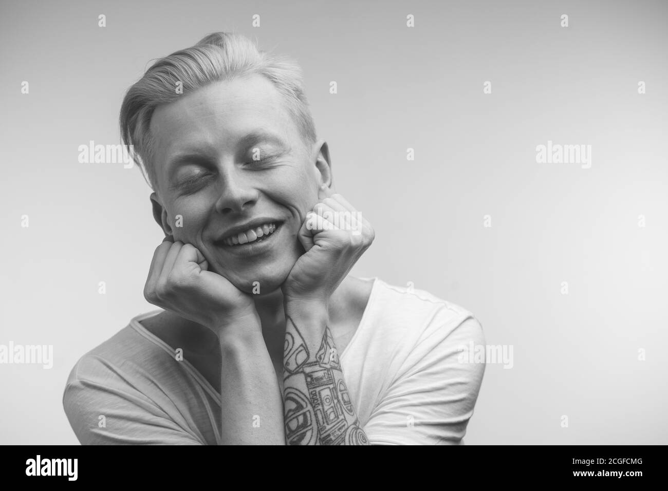 Monochrome shot of happy blonde man with uncommon handsome appearance smiling into camera having pleased dreaming expression being happy with coming h Stock Photo