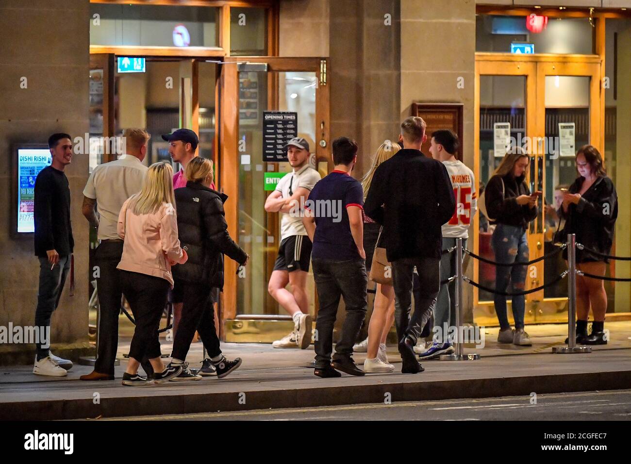 Young people queue to get into a pub in Cardiff city centre at night. A ban on groups of more than six people meeting indoors in Wales, including pubs and restaurants, is expected to be announced later today as ministers try to tackle the rising number of coronavirus cases across the UK. Stock Photo