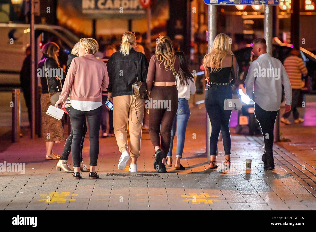 A group of young adults walk through Cardiff city centre at night. A ban on groups of more than six people meeting indoors in Wales, including pubs and restaurants, is expected to be announced later today as ministers try to tackle the rising number of coronavirus cases across the UK. Stock Photo