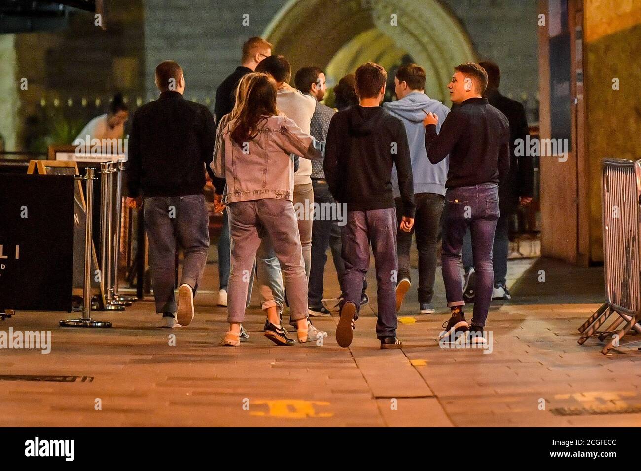 A group of young people walk through Cardiff city centre at night. A ban on groups of more than six people meeting indoors in Wales, including pubs and restaurants, is expected to be announced later today as ministers try to tackle the rising number of coronavirus cases across the UK. Stock Photo