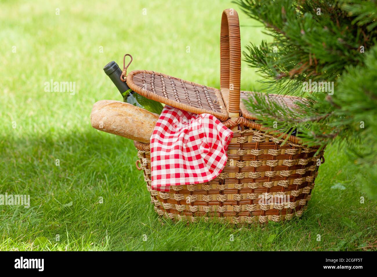 Picnic basket with wine and baguette on garden sunny grass Stock Photo