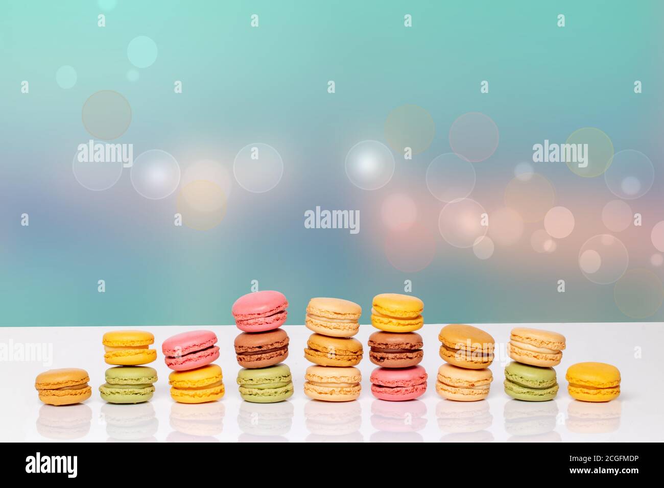 Macaron pyramids. Close-up of colourful French macaroons in shape of a pyramid on a white table against abstract bright pastel colored background. Adv Stock Photo