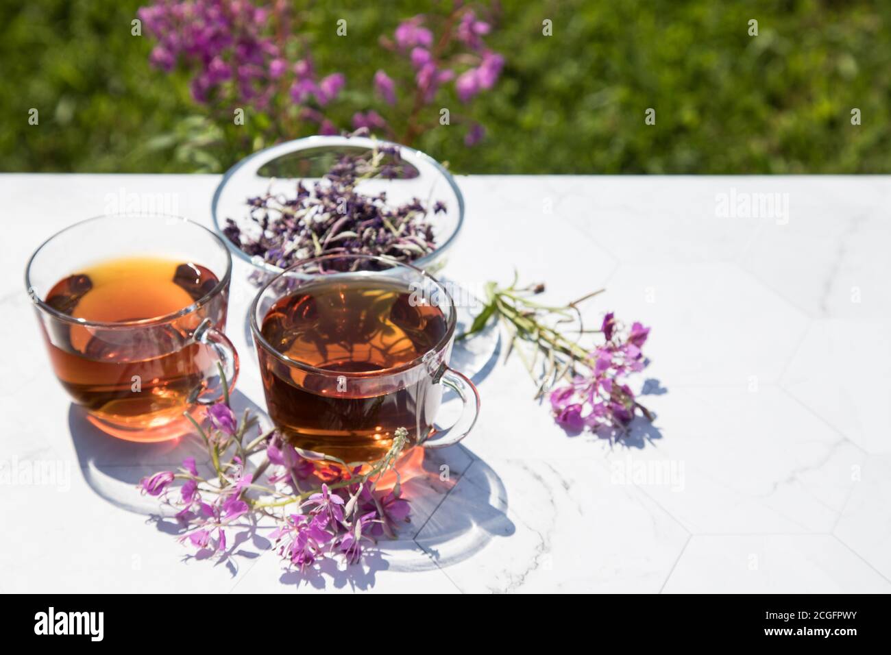 Chamaenerion angustifolium tea (cypress, big willow, pink willow) with dry and fresh flowers for decoration in glass cups on a light background. Conce Stock Photo