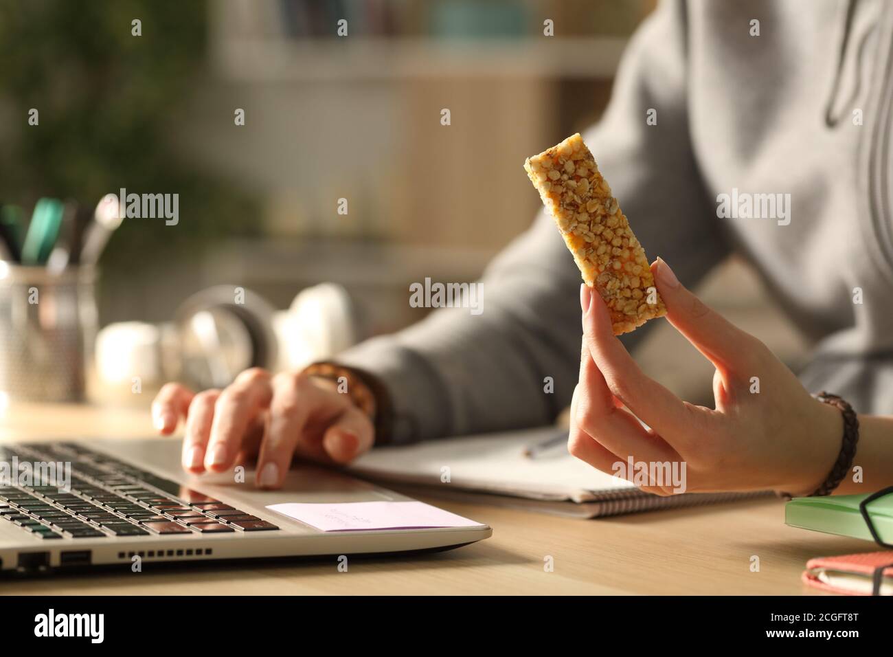 Close up of student girl hands holding snack bar at night elearning on laptop Stock Photo