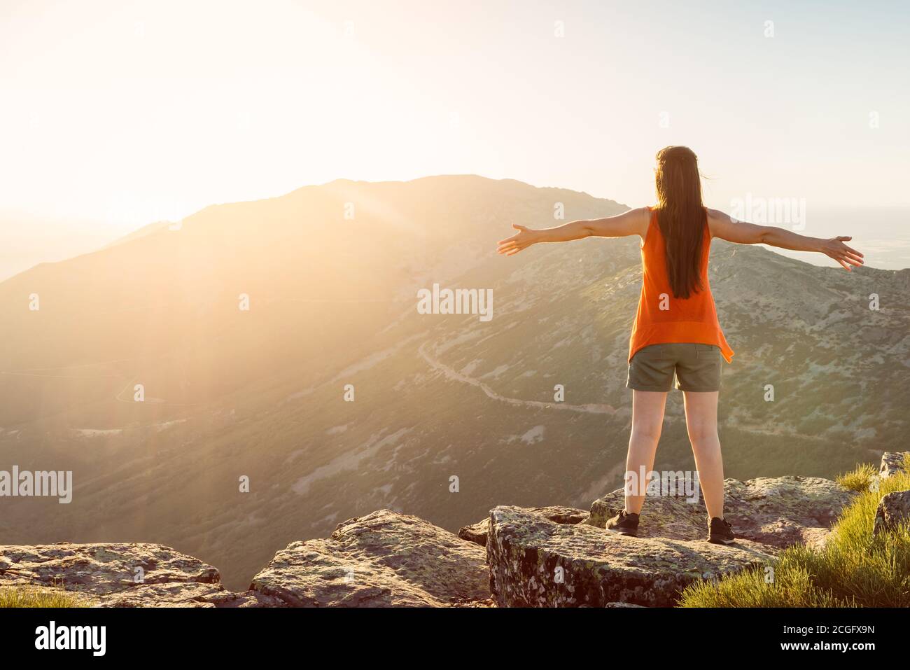 Happy woman with open arms stay on the peak of the mountain cliff edge under sunset light Stock Photo