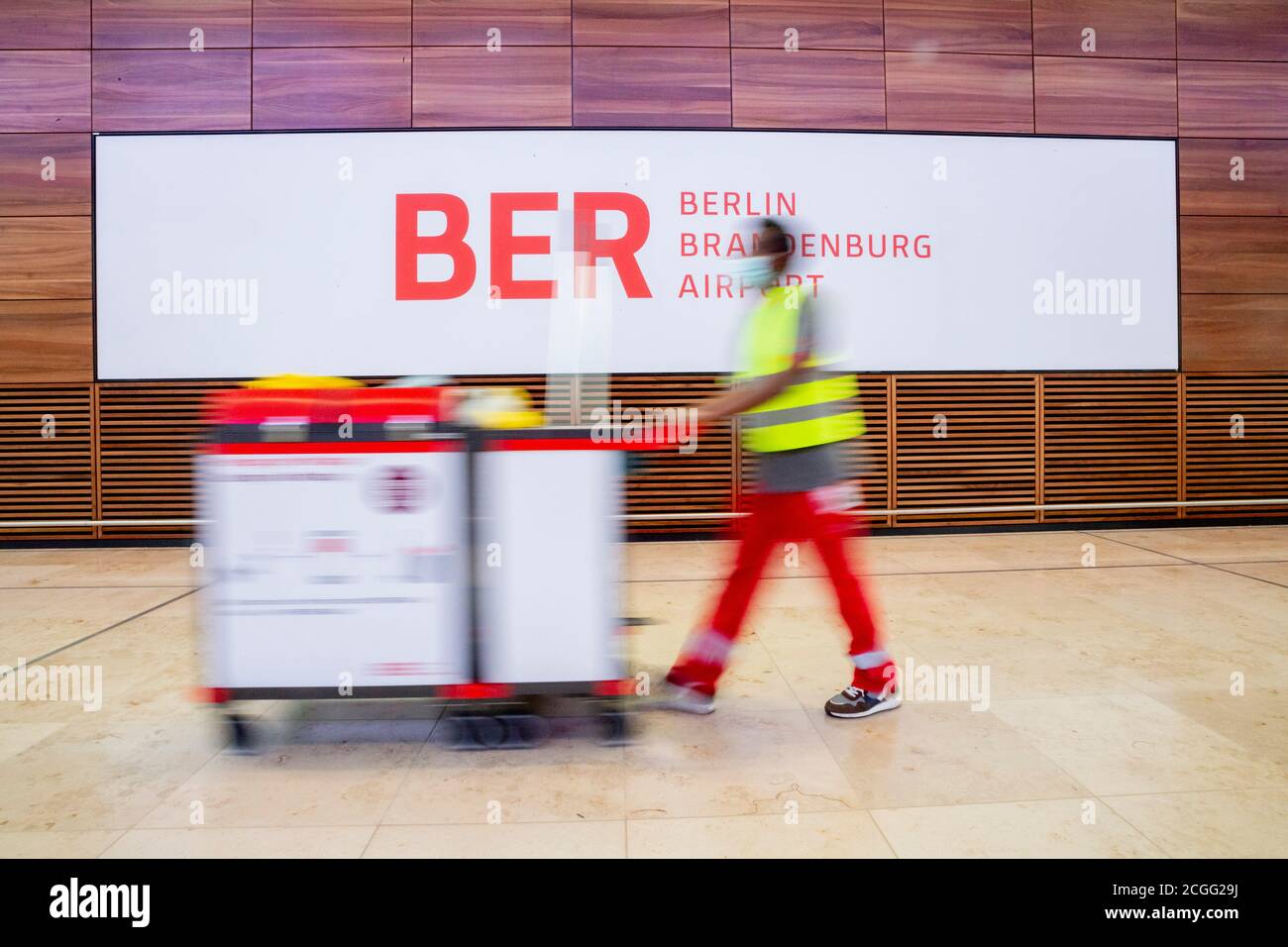 08 September 2020, Brandenburg, Schönefeld: A building cleaner pushes his trolley in front of the BER logo during a tour of Berlin Brandenburg Airport 'Willy Brandt' (BER) in Terminal T1. The capital city airport is scheduled to open on 31 October 2020. (motion blur due to long exposure time) Photo: Christoph Soeder/dpa Stock Photo