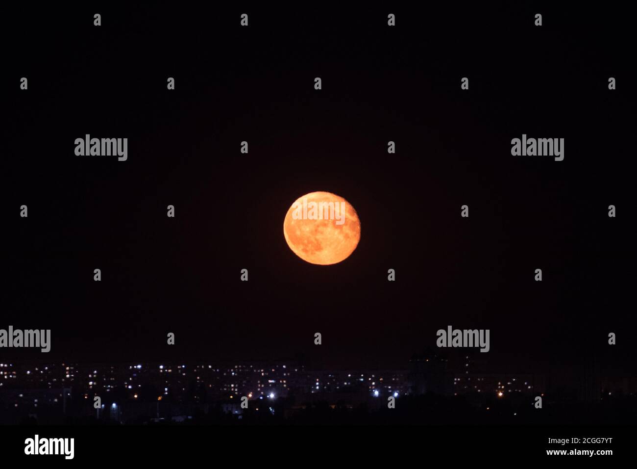 Bright big orange full moon rising up on dark night sky above city lights. Mystic nighttime black sky with large moon, dark tranquility Stock Photo